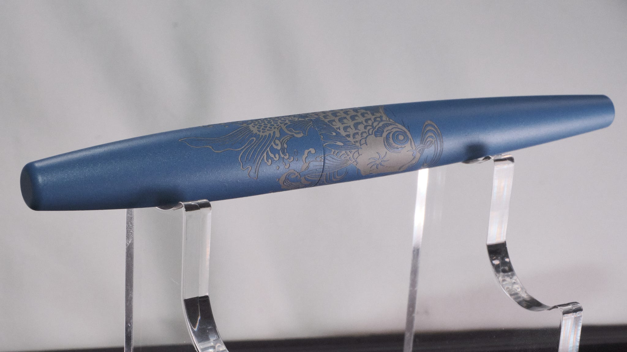 Photo of a pale blue capped fountain pen with an intricate Koi fish engraved on the body.