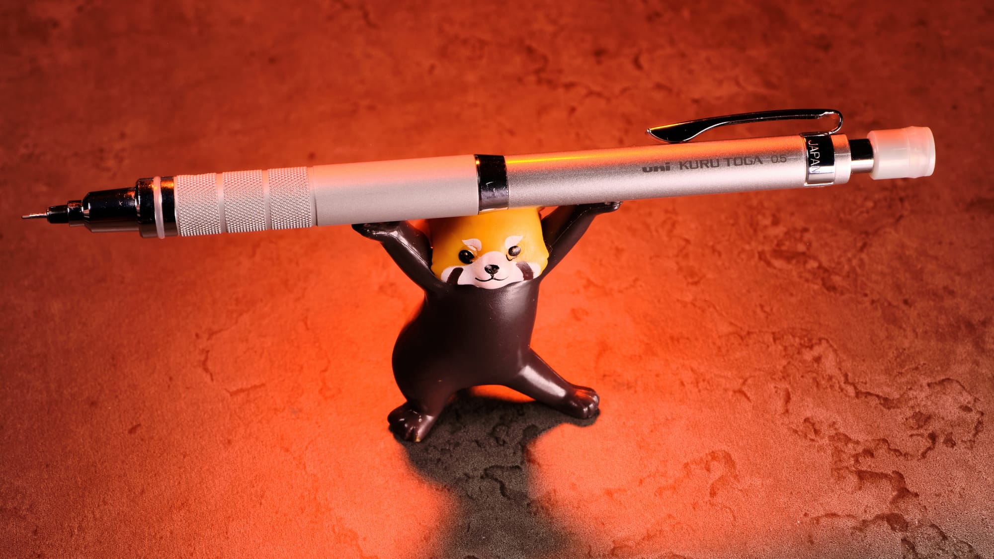 Photo of the Kuru Toga Roulette being held up by a Red Panda figure, with an orange marbled background