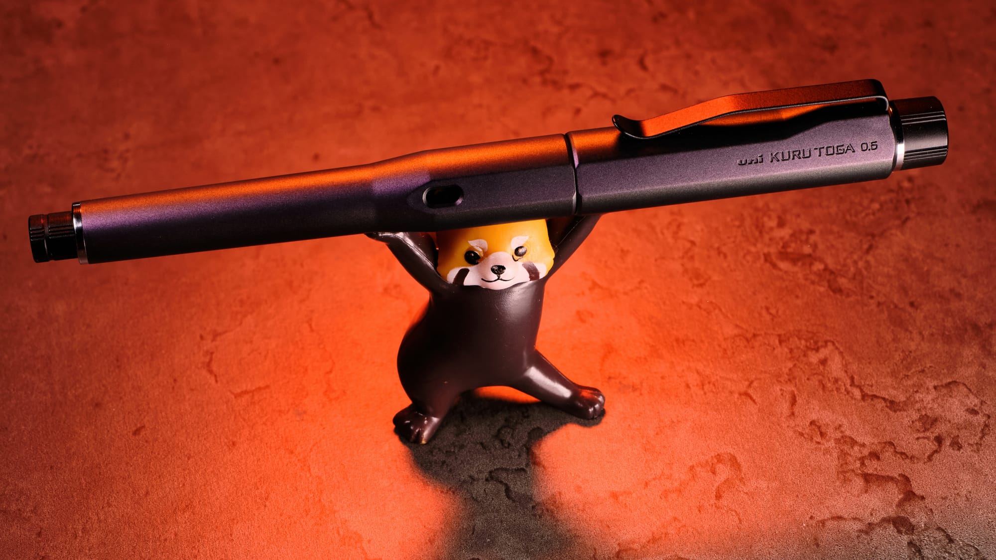 Photo of the Kuru Toga Dive being held up by a Red Panda figure, with an orange marbled background