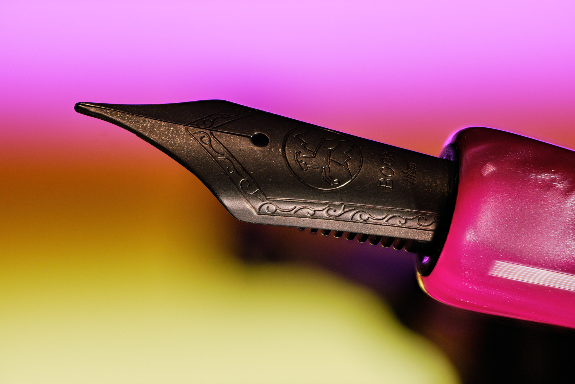 Close-up photo of the JG6's Titanium nib, in front of a blurred background with a magenta to yellow gradient.