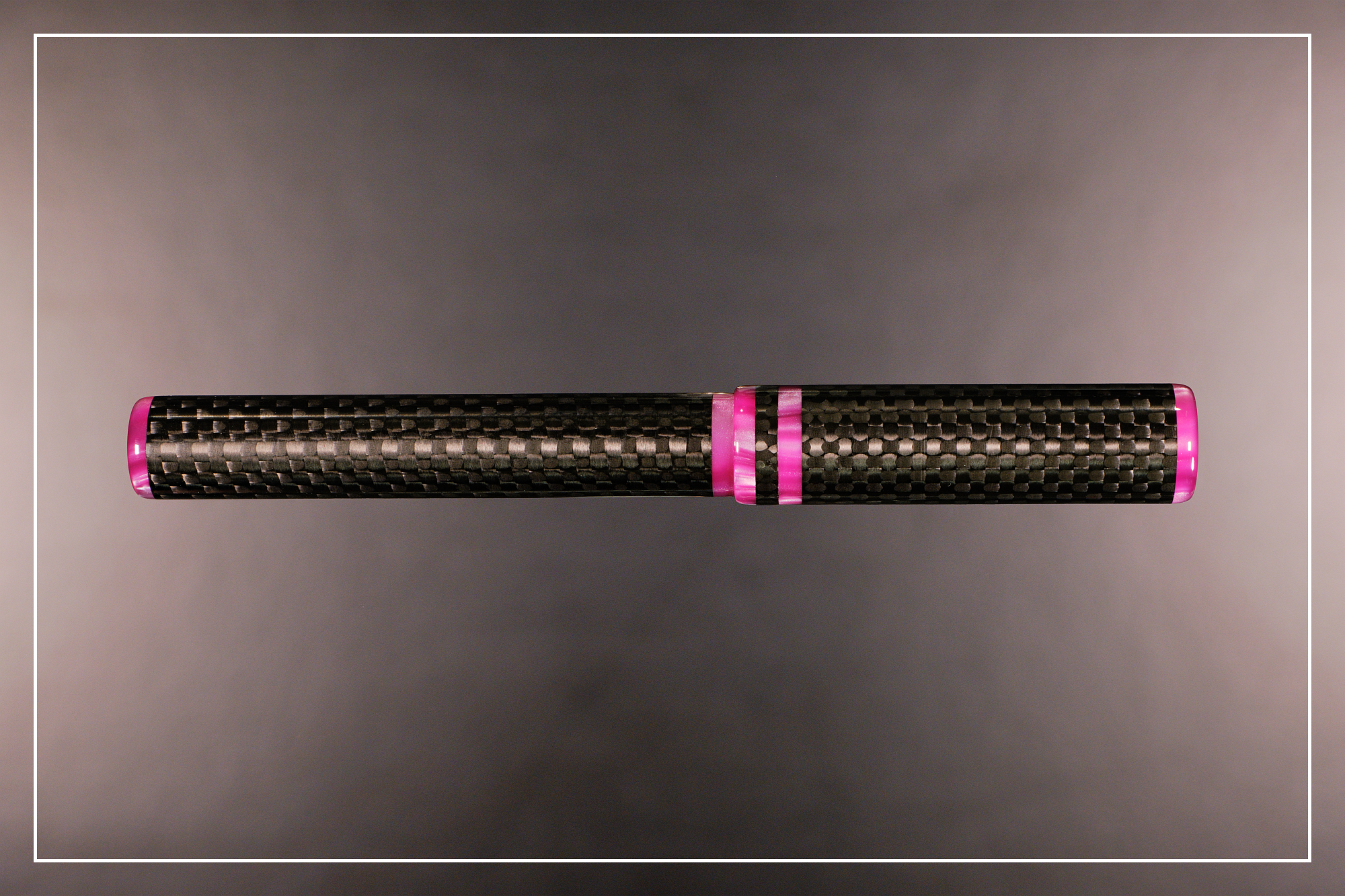 Photo of the carbon fibre & magenta JG6 fountain pen on a blurred grey background.