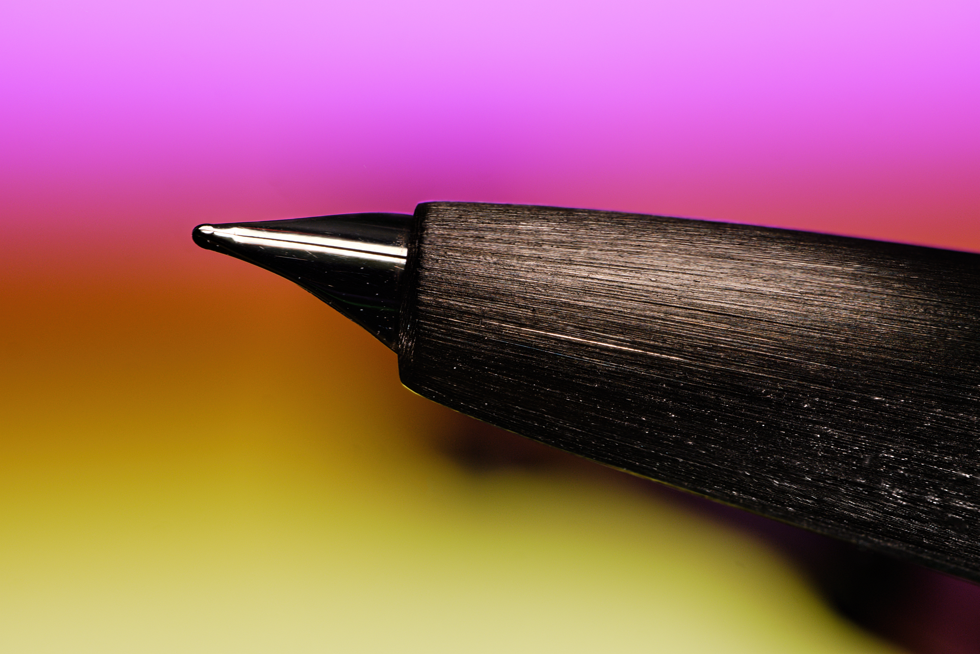 Close-up of the Lamy 2000's 14k platinum-coated 14k gold nib, in front of a blurred background with a magenta to yellow gradient.