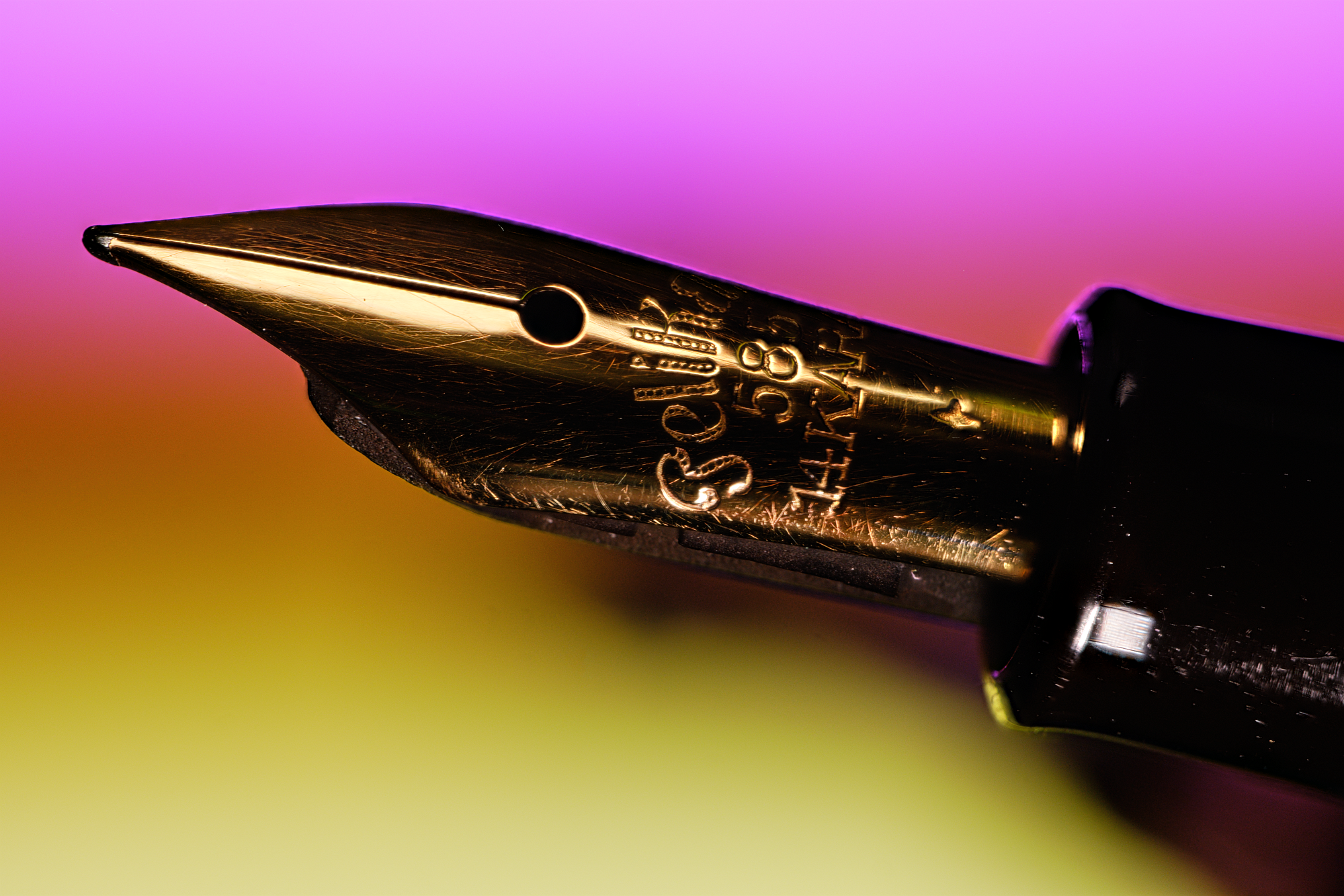 Close-up photo of the Pelikan 400's 14k gold nib, in front of a blurred background with a magenta to yellow gradient.