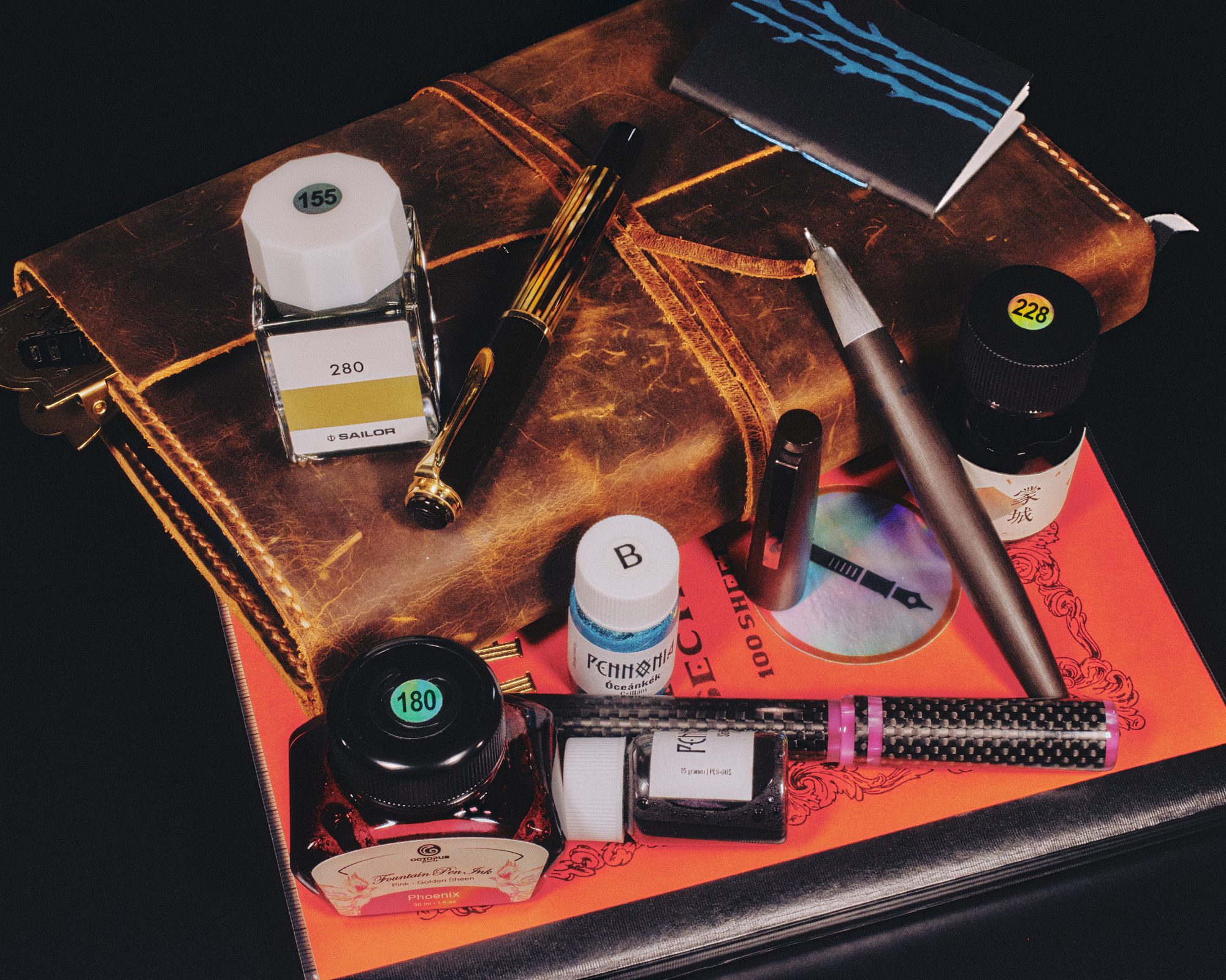 Photo of a pile of notebooks, leather-bound journal, fountain pens, & ink bottles.