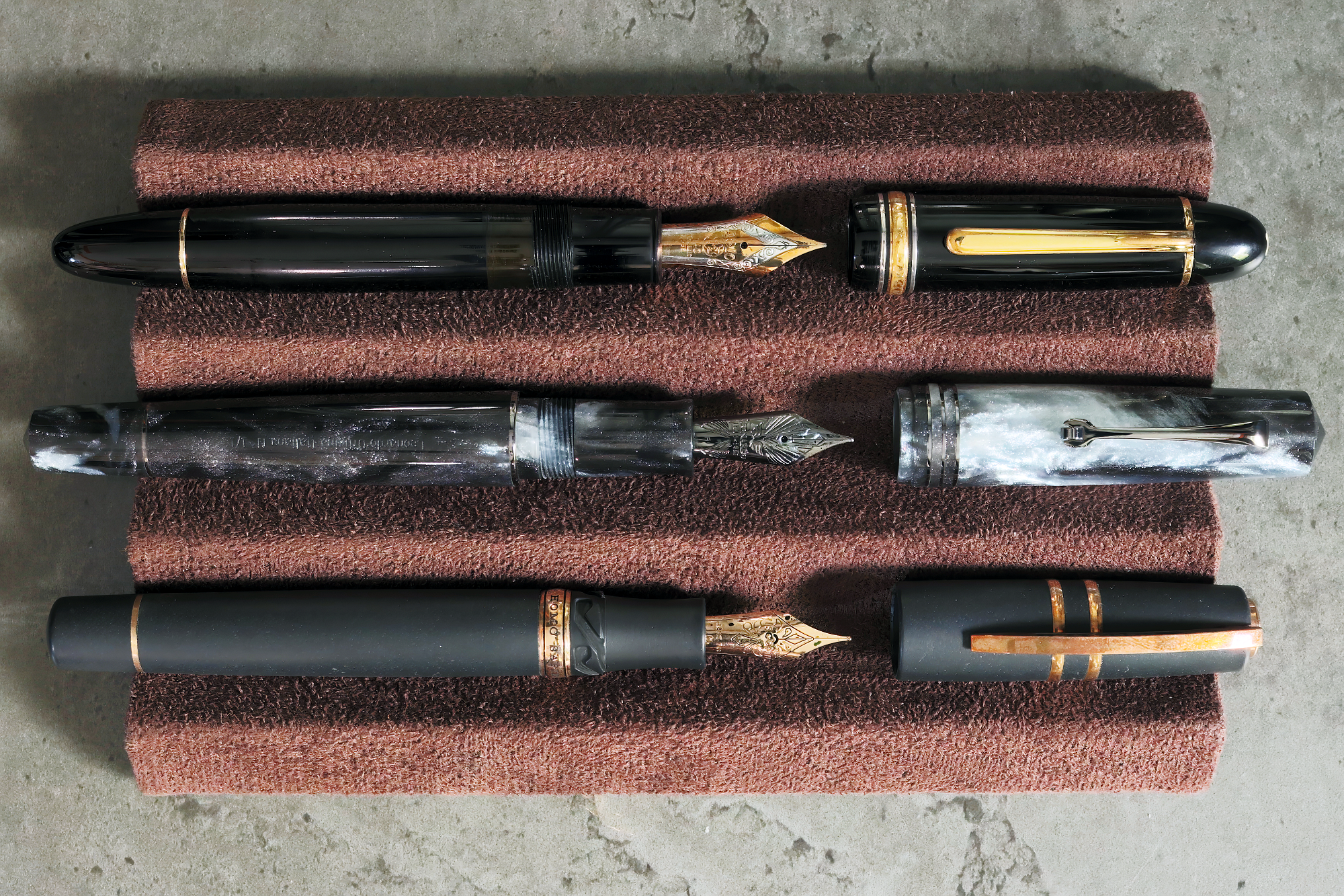 Photo showing my previous pen rental with their caps off on a brown pen display over a grey marble background.