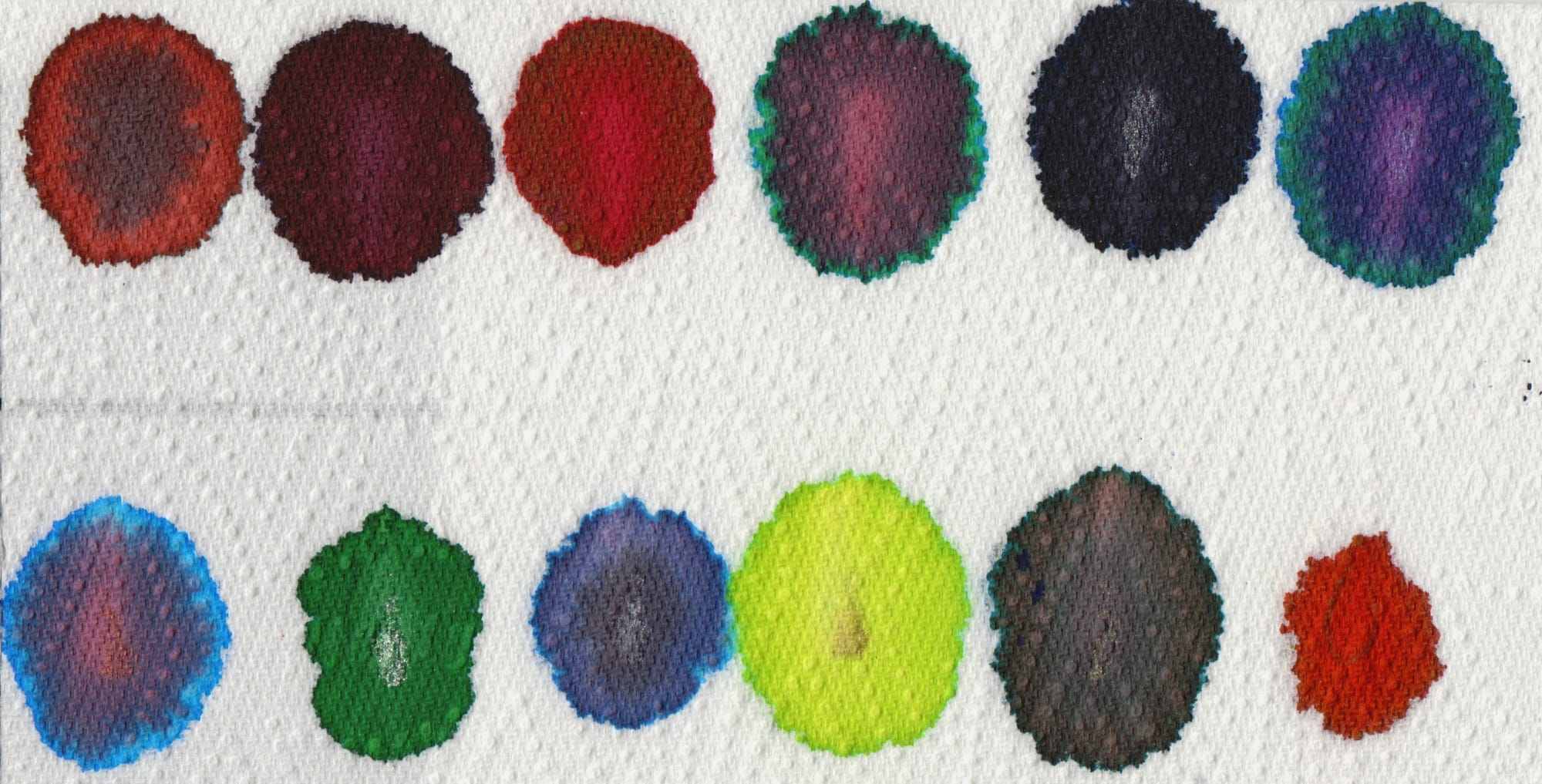 Various colours of ink splotches on a paper towel. Some of the inks can been seen to separate out into their component colours.