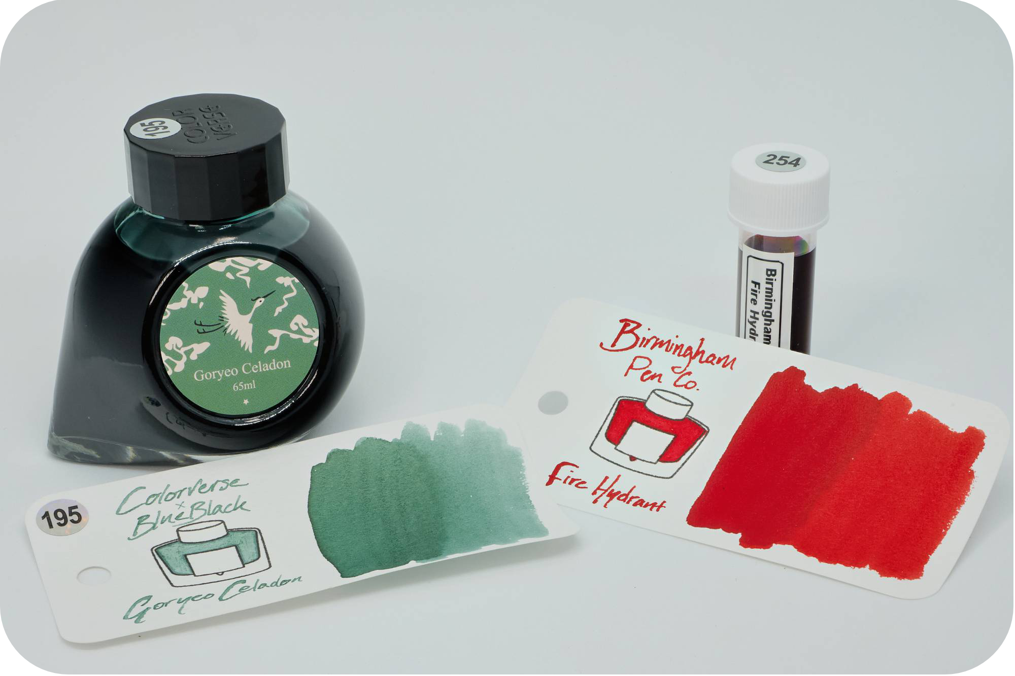 Photo of a bottle of ColorVerse Goryeo Celadon ink & a sample vial of Birmingham Pen Co Fire Hydrant with their respective swatches in front on a white background