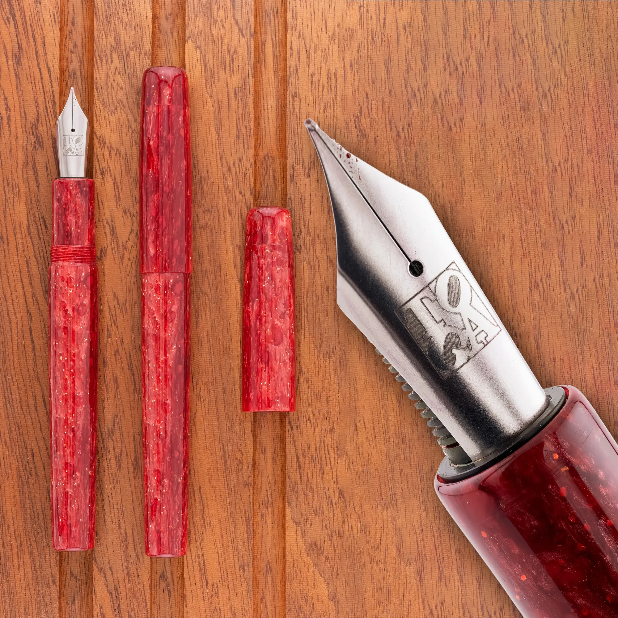 Overhead photo of a sparkly red acrylic fountain pen on a wooden tray. The pen is shown capped and uncapped, along with a close-up of the nib.