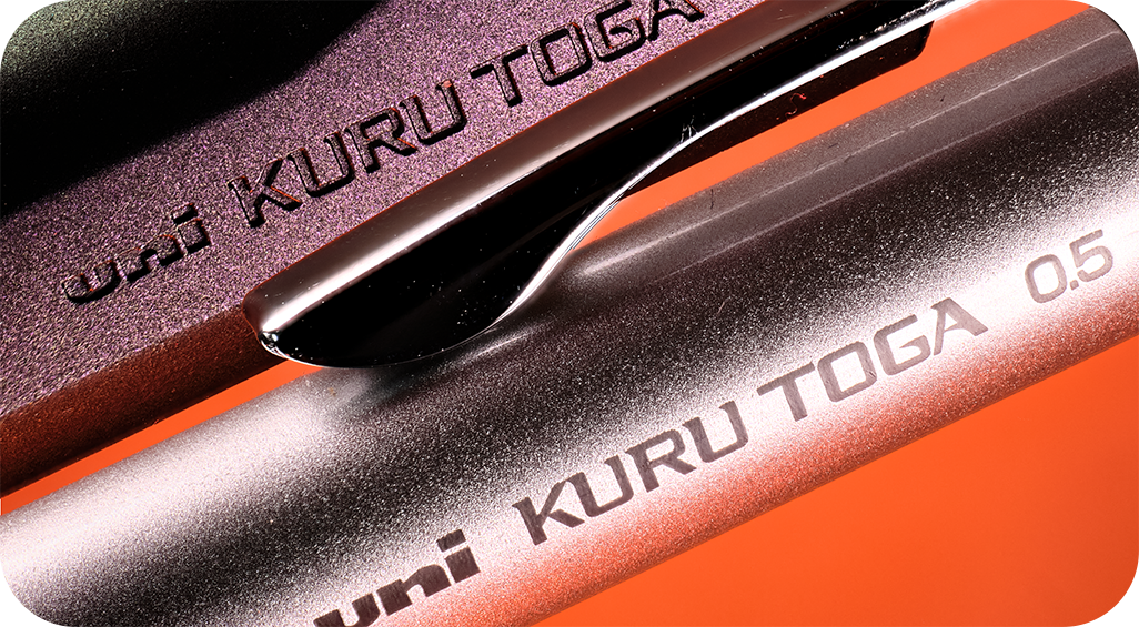 Close up image of 2 Uni Kuru Toga mechanical pencils showing the name imprints with an orange background.