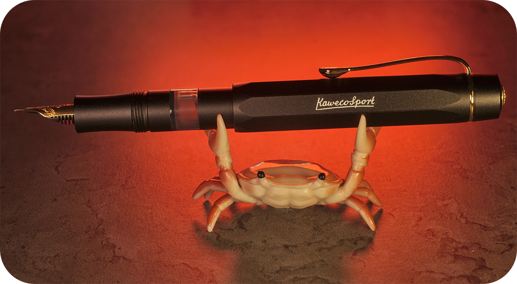Photo of a model crab holding a matte black Kaweco Sport Piston Filler with the cap posted.