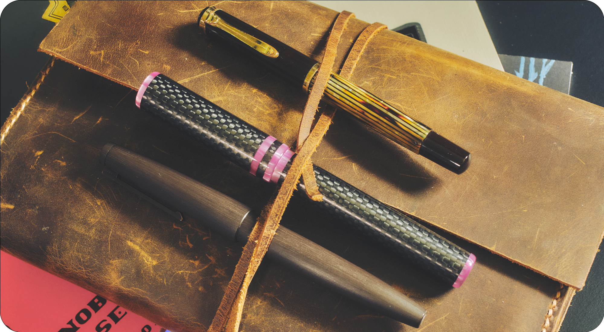 3 capped fountain pens in top of a pile of notebooks