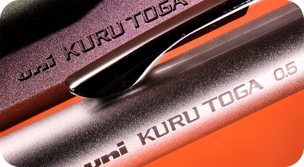 Close up image of 2 Uni Kuru Toga mechanical pencils showing the name imprints with an orange background.