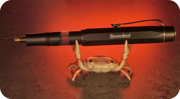 Photo of a model crab holding a matte black Kaweco Sport Piston Filler with the cap posted.