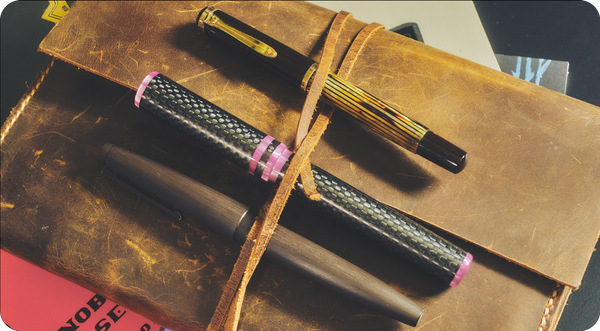 3 capped fountain pens in top of a pile of notebooks